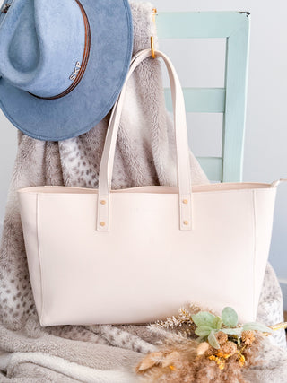 White tote bag with a blue hat and gray scarf on a wooden surface