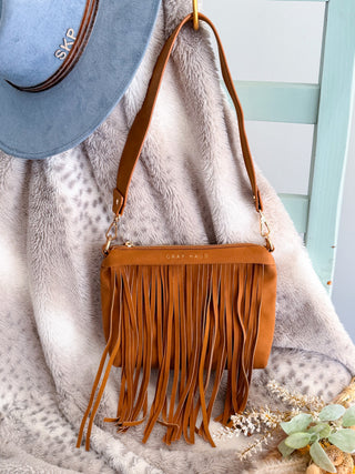 Brown fringe handbag on a textured surface with a blurred background