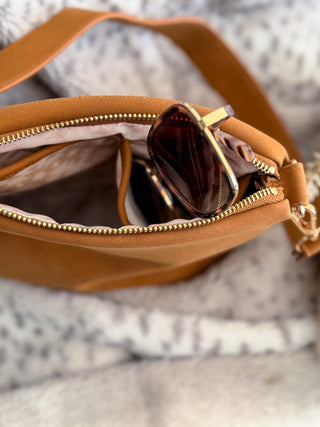 Brown leather bag with sunglasses inside on a textured surface