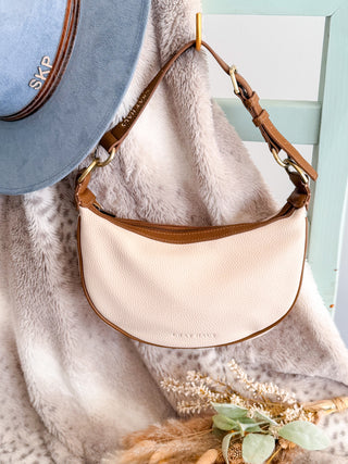 Beige handbag with brown handle on a textured surface with a light blue background