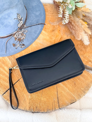Black clutch bag on a wooden surface with a blue hat and decorative elements.