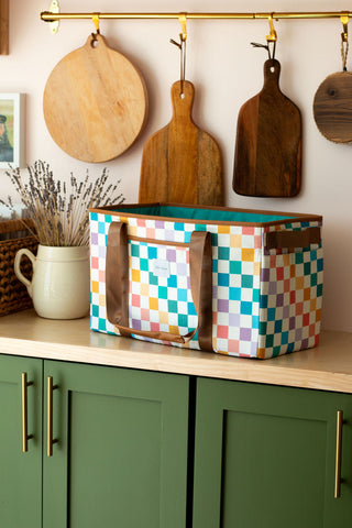 Colorful checkered basket on a kitchen counter with wooden cutting boards and green cabinets.