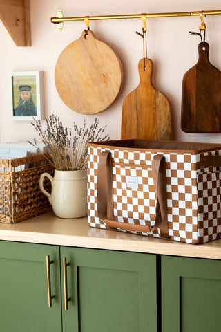 Wooden cutting boards and a checkered basket on a kitchen counter with green cabinets.