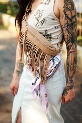 Person wearing a beige fringed bag with tattoos on arms and legs.