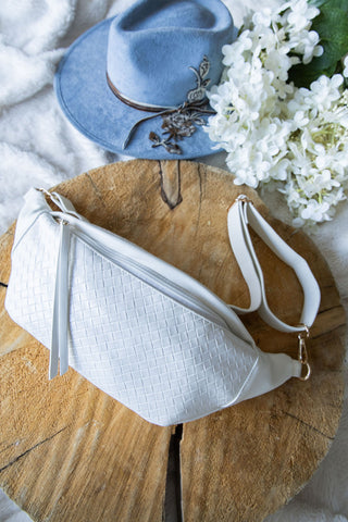 White woven handbag with a blue hat and white flowers on a wooden surface