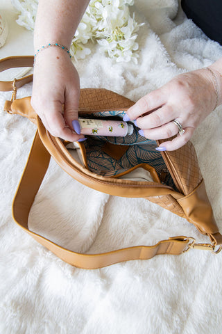 Person organizing items in a brown leather bag on a white surface with flowers in the background