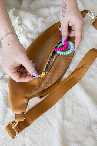Brown leather bag with colorful hair ties on a fluffy white surface