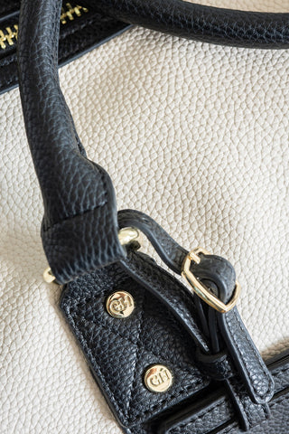 Close-up of a black leather handbag handle with gold hardware on a light beige background