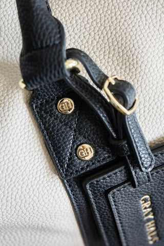 Close-up of a black leather handbag with gold hardware on a light gray background