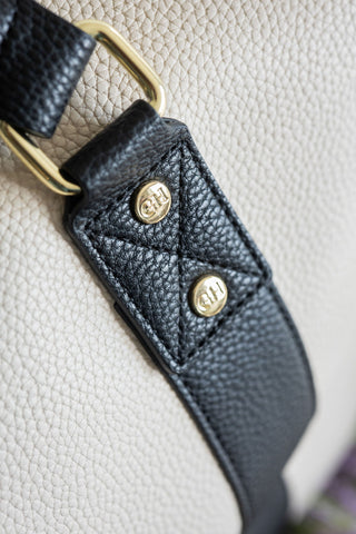 Close-up of a black leather strap with gold hardware on a beige background