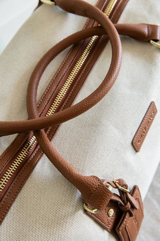 Close-up of a beige handbag with brown leather handles and zipper.