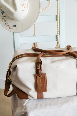 Beige duffel bag with brown accents and a matching hat on a white surface.