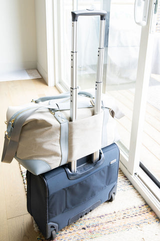 Blue suitcase with a beige duffel bag on top near a window.