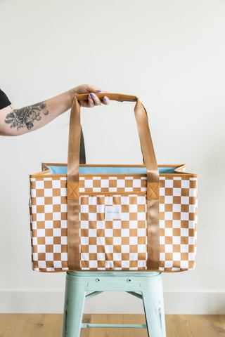 Person holding a checkered tote bag with a tattooed arm on a white background