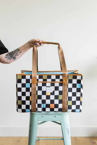 Person holding a checkered bag with brown handles on a light blue stool against a white background