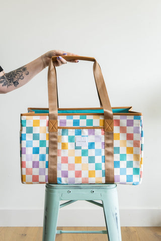 Colorful checkered tote bag held above a green stool against a white background