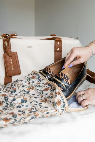 Person placing a leopard print shoe into a floral-patterned bag with a white background.
