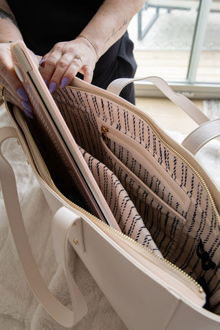 Beige handbag with interior compartments being held open, showing a patterned lining.