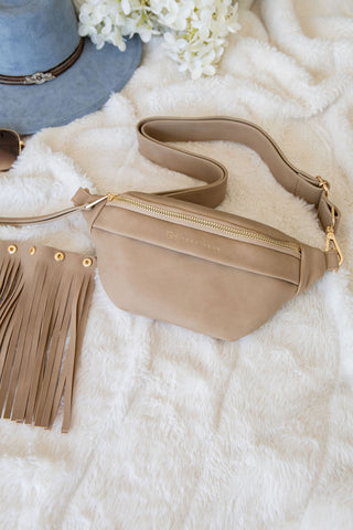 Beige fanny pack with fringe details on a white fur surface