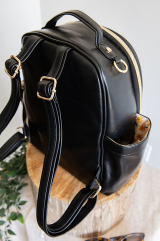 Black leather backpack on a wooden surface with a white background