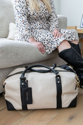 Person sitting on a couch with a beige duffel bag in front of them